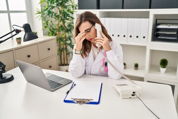 Young woman wearing doctor uniform stressed talking on the telephone at clinic