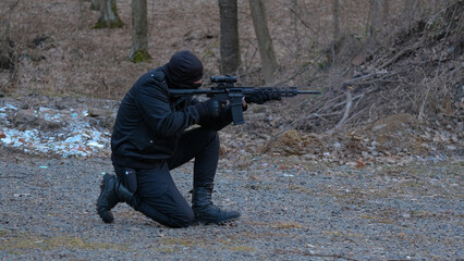 A soldier of a special unit in a black uniform shoots an assault rifle at a training ground