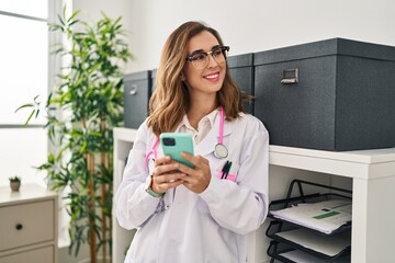 Young woman wearing doctor uniform using smartphone at clinic