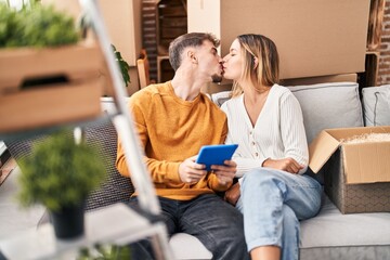 Young man and woman couple using touchpad sitting on sofa at new home