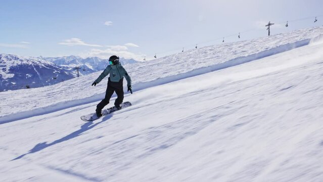 Slow motion of piste snowboarder running down hill. 4K skiing footage, one man snowboarder snowboarding on ski slope on sunny winter day with clear blue sky in European alps mountains, Austria.