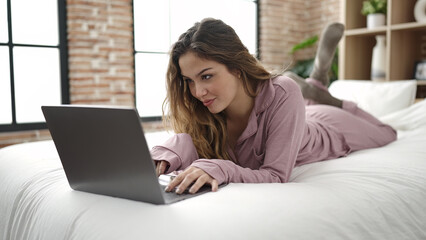 Young beautiful hispanic woman using laptop lying on bed at bedroom