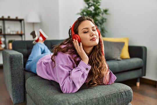 Young beautiful hispanic woman listening to music lying on sofa at home