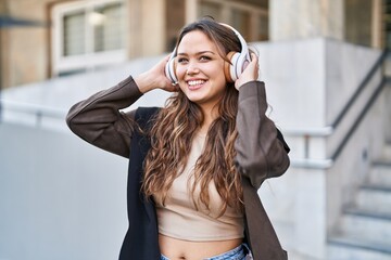 Young beautiful hispanic woman listening to music standing at street