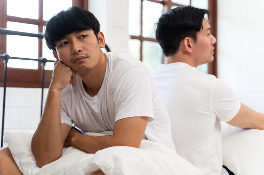 LGBT couple quarrel sitting on different sides of the bed. Men who are lovers are having problems or do not understand each other in stressful, angry moods in lgbt couple concept.