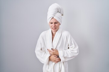 Blonde caucasian woman wearing bathrobe with hand on stomach because indigestion, painful illness feeling unwell. ache concept.