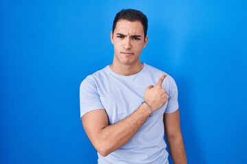 Young hispanic man standing over blue background pointing aside worried and nervous with forefinger, concerned and surprised expression