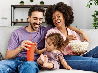 Couple and daughter watching movie sitting on sofa at home