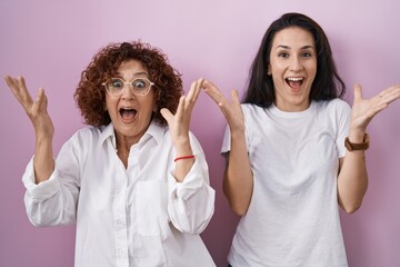 Hispanic mother and daughter wearing casual white t shirt over pink background celebrating crazy...