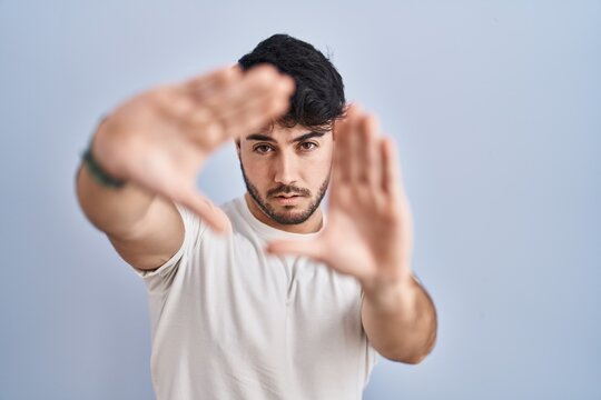 Hispanic man with beard standing over white background doing frame using hands palms and fingers, camera perspective