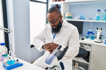 Young african american man wearing scientist uniform looking watch at laboratory