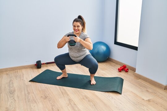 Young beautiful plus size woman using kettlebell training legs exercise at sport center