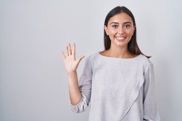Young hispanic woman standing over white background showing and pointing up with fingers number...