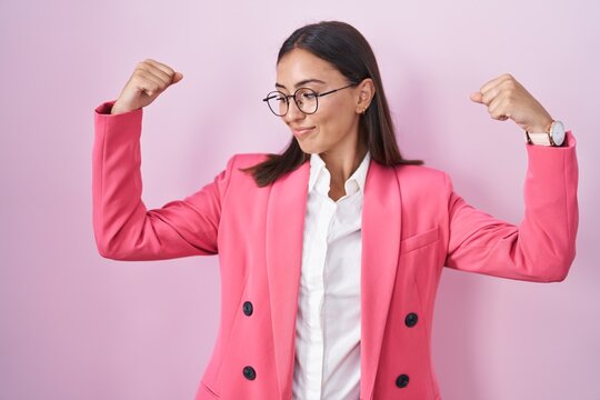 Young hispanic woman wearing business clothes and glasses showing arms muscles smiling proud. fitness concept.