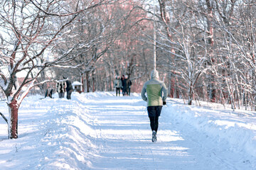 A man in sportswear runs along the road in a winter park
