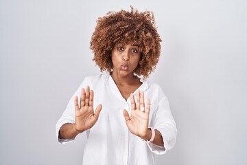 Young hispanic woman with curly hair standing over white background moving away hands palms showing...