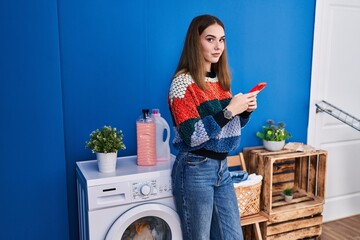 Young woman using smartphone waiting for washing machine at laundry room