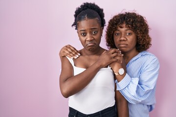 Obraz premium Two african women standing over pink background depressed and worry for distress, crying angry and afraid. sad expression.