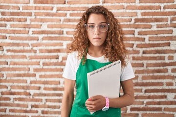 Young caucasian woman holding art notebook relaxed with serious expression on face. simple and natural looking at the camera.