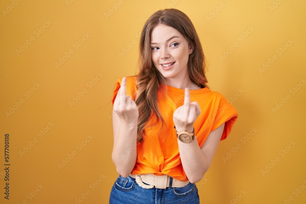 Poster caucasian woman standing over yellow background showing middle finger doing fuck you bad expression,