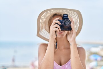 Fototapeta na wymiar Young blonde woman tourist smiling confident using professional camera at seaside