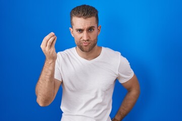 Young caucasian man standing over blue background doing italian gesture with hand and fingers confident expression