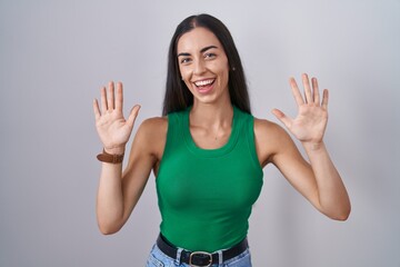 Young woman standing over isolated background showing and pointing up with fingers number ten while smiling confident and happy.