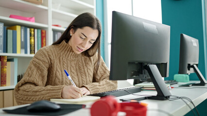 Young beautiful hispanic woman student using computer taking notes at university classroom