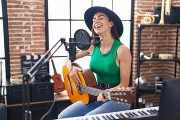 Fototapeta na wymiar Young hispanic woman musician singing song playing classical guitar at music studio