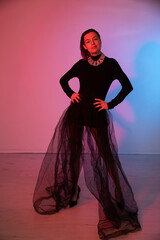 a woman in black clothes in a tulle skirt poses on a pink background