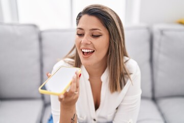 Young hispanic woman talking on the smartphone sitting on sofa at home