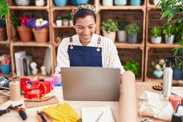 Young beautiful hispanic woman florist smiling confident using laptop at florist