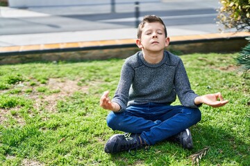 Naklejka na ściany i meble Blond child doing yoga exersice sitting on grass at park