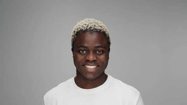 Portrait of Young Black Man Looking at Camera in Color Studio Shot. Adult Afro Boy Isolated Alone on Grey Background Close up. African American 20s Person has Beautiful Bright Eyes and Smiling Happy