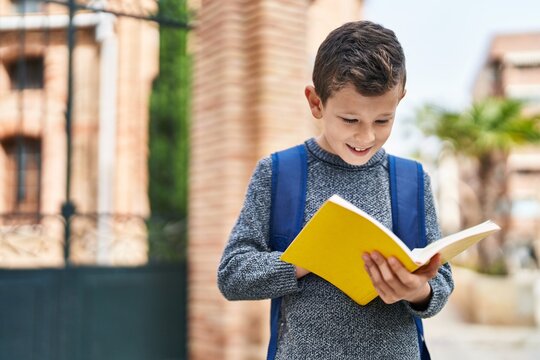 Blond child student reading book standing at street