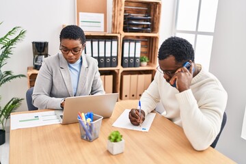 Man and woman business workers using laptop and talking on the smartphone at office