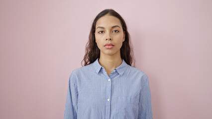 Young beautiful hispanic woman standing with serious expression over isolated pink background