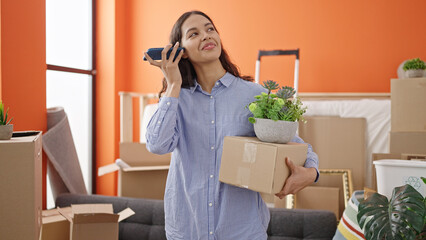 Fototapeta na wymiar Young beautiful hispanic woman listening to voice message with smartphone holding a box at new home