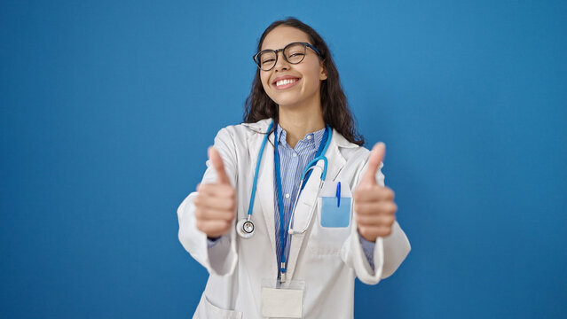 Young beautiful hispanic woman doctor doing thumbs up over isolated blue background