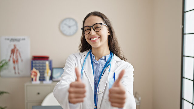 Young beautiful hispanic woman doctor doing thumbs up at clinic