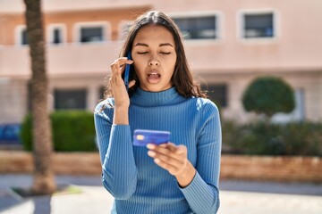 Young african american woman talking on the smartphone and holding credit card at park