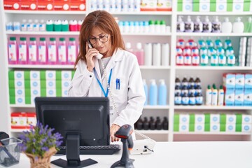 Middle age woman pharmacist talking on telephone using computer at pharmacy