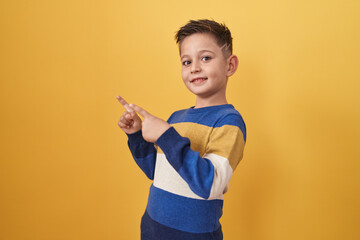 Little hispanic boy standing over yellow background smiling and looking at the camera pointing with...