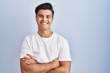 Fototapeta premium Hispanic man standing over blue background happy face smiling with crossed arms looking at the camera. positive person.