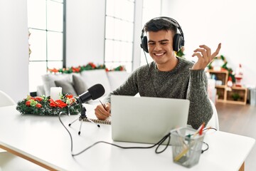 Young hispanic man radio worker working sitting by christmas tree at home