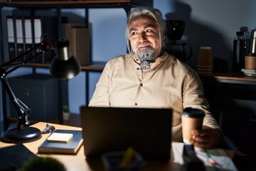 Middle age man with grey hair working at the office at night smiling looking to the side and staring away thinking.