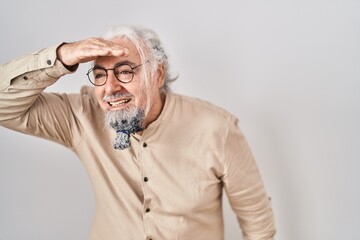 Middle age man with grey hair standing over isolated background very happy and smiling looking far away with hand over head. searching concept.