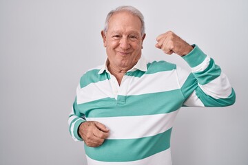 Senior man with grey hair standing over white background strong person showing arm muscle, confident and proud of power