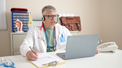 Middle age grey-haired man doctor having online medical consultation at clinic