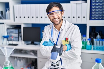Young hispanic man scientist smiling confident with arms crossed gesture at laboratory